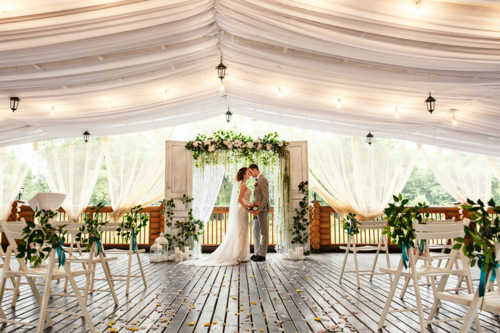 Adobe Stock - Photo d'illustration - Un couple de mariés prend la pose devant une arche de cérémonie nuptiale faite à l'aide de portes.