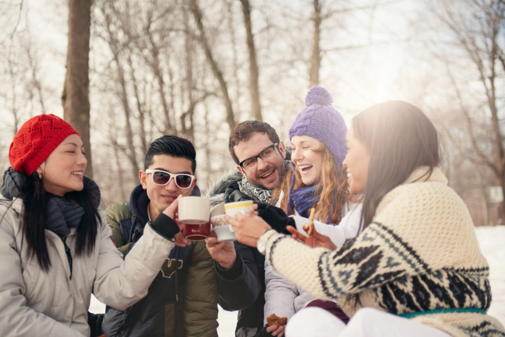 Adobe Stock - Photo d'illustration - Un groupe d'amis trinque et boit des cocktails dans des tasses. Ils profitent de l'hiver et de ses extérieurs enneigés pour les savourer.