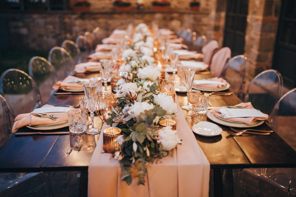 Adobe Stock - Photo d'illustration - Une nappe blanche, placée comme un chemin de table et recouverte de fleurs et branches d'eucalyptus, pare une table de repas de mariage.