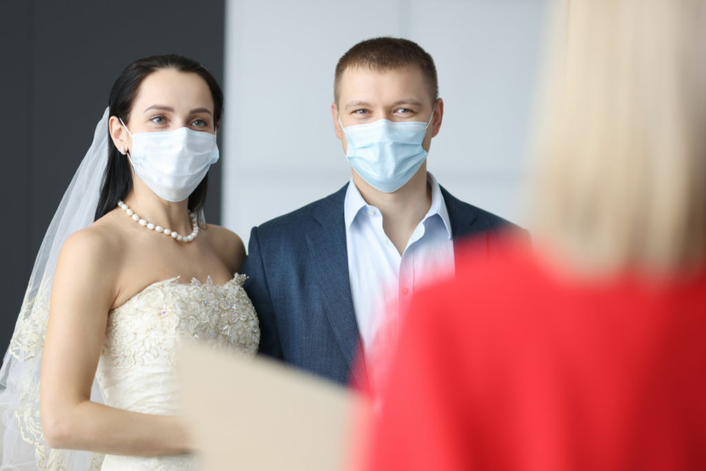 Adobe Stock - Photo d'illustration - Forcé de composer avec le coronavirus, un couple, masque sur le visage, échange ses vœux de mariage devant le maire.