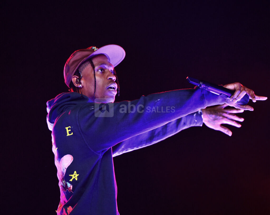 Creative Commons - Le rappeur américain Travis Scott, habillé d'une casquette et d'un sweat à capuche. Il tient un micro dans sa main droite. L'artiste, faisant fi des normes de sécurité, est accusé d'avoir poussé au débordement durant son festival, ce qui a conduit 8 de ses fans à perdre la vie.