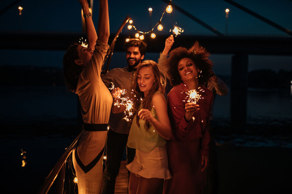 Adobe Stock - photo d'illustration - Des amis font la fête et tiennent des cierges magiques qui les illuminent, comme les étoiles dans le ciel.
