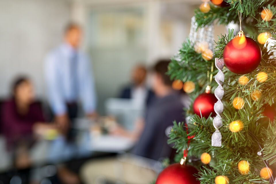Adobe Stock - Photo d'illustration - Un sapin de Noël décoré dans un bureau avec l'équipe de travail en fond