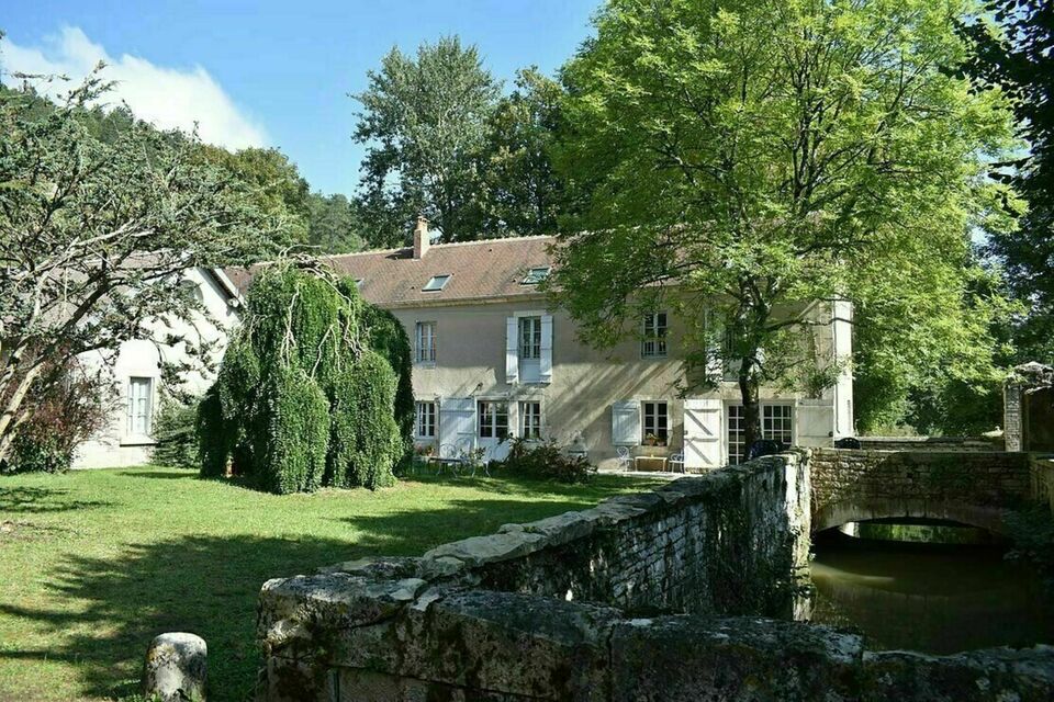 ABC Salles - Le domaine des Douves, on y voit la grande bâtisse entourée de verdure, il y a un pont en pierre sur le côté droit.