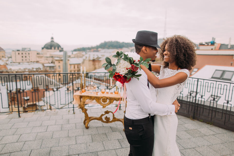 Adobe Stock - Deux époux sur le toit d'un immeuble, la mariée à les cheveux frisé et une robe à manche courte.