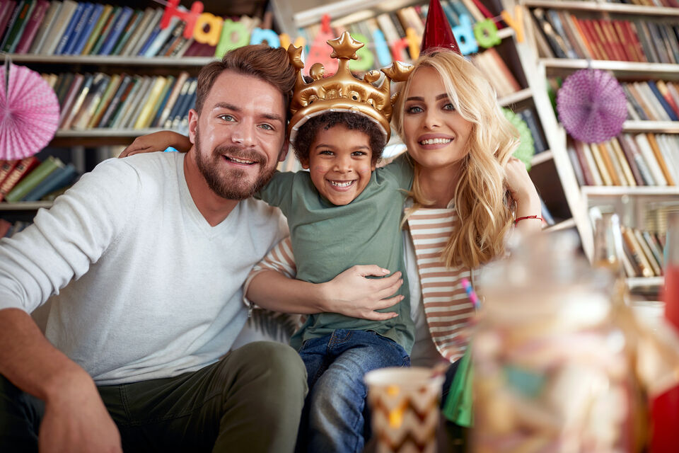 Adobe Stock - photo d'illustration - A gauche, il y a le père. Un homme blanc, aux yeux bleu. Au centre, il y a un enfant à la peau mate avec une couronne sur la tête. À droite, il y a la mère. Une femme blanche, blonde aux yeux bleu. L'enfant semble avoir été adopté.<br>