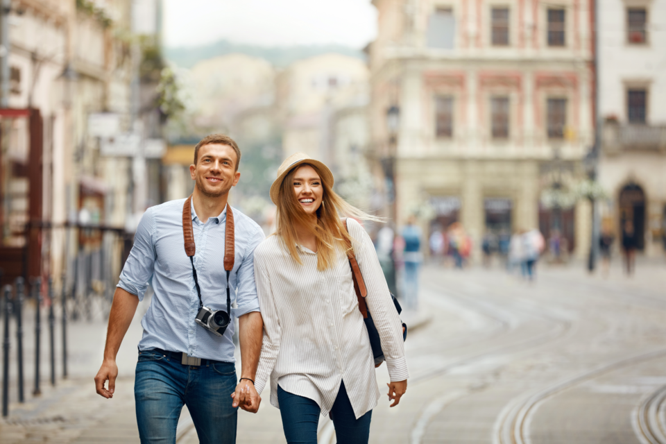 Adobe Stock - Un couple se baladant en se tenant la main. L'homme a un appareil photo autour du cou et la femme, elle, porte un sac à dos.