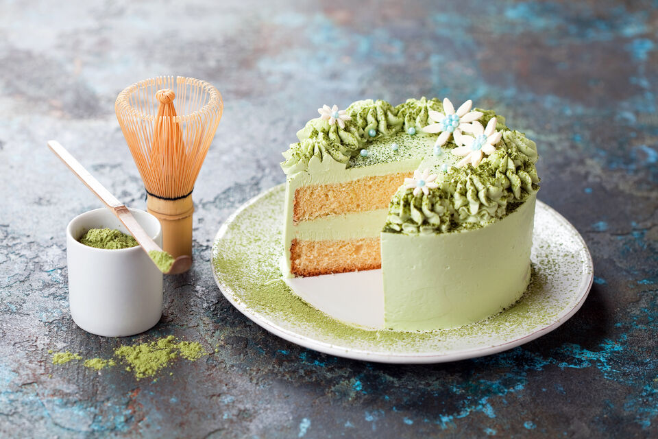 Adobe Stock - Un gâteau au matcha, où l'on voit qu'une part de gâteau a déjà été coupée. À sa gauche, il y a un ramequin avec de la poudre de matcha et un chasen, sorte de fouet en bambou.