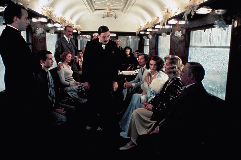 Allociné - Image tirée du film Le crime de l'Orient-Express. On y voit des homme et des femmes assis dans un wagon, avec un homme debout au centre.