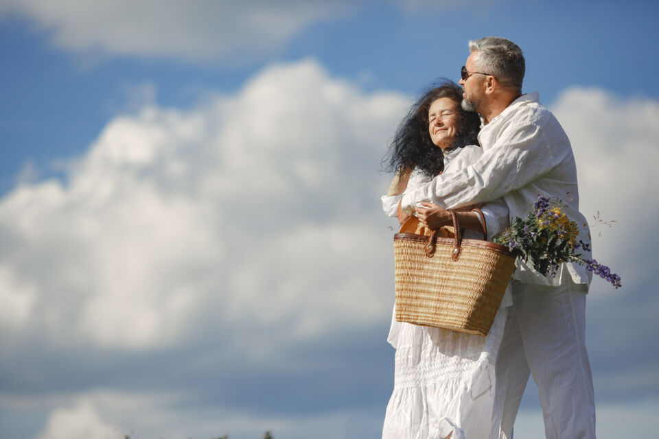 Freepik - Photo d'illustration - Un couple épanoui, vêtu élégamment de blanc, se promène  à l'extérieur, célébrant leurs noces d'ivoire avec amour et tendresse. Leur étreinte et leurs sourires radieux témoignent de 62 années de bonheur partagé.