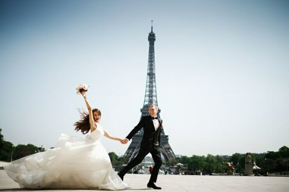 Freepik - Photo d'illustration - Jeunes mariés en joie, main dans la main, célébrant leur amour sous le regard emblématique de la Tour Eiffel, symbole de romance à Paris.