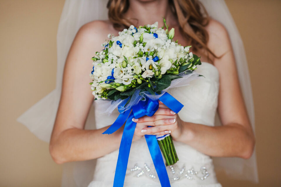 Freepik - Photo d’illustration : La mariée porte un bouquet de fleurs orné de rubans bleus, symboles de chance et de bonheur. 