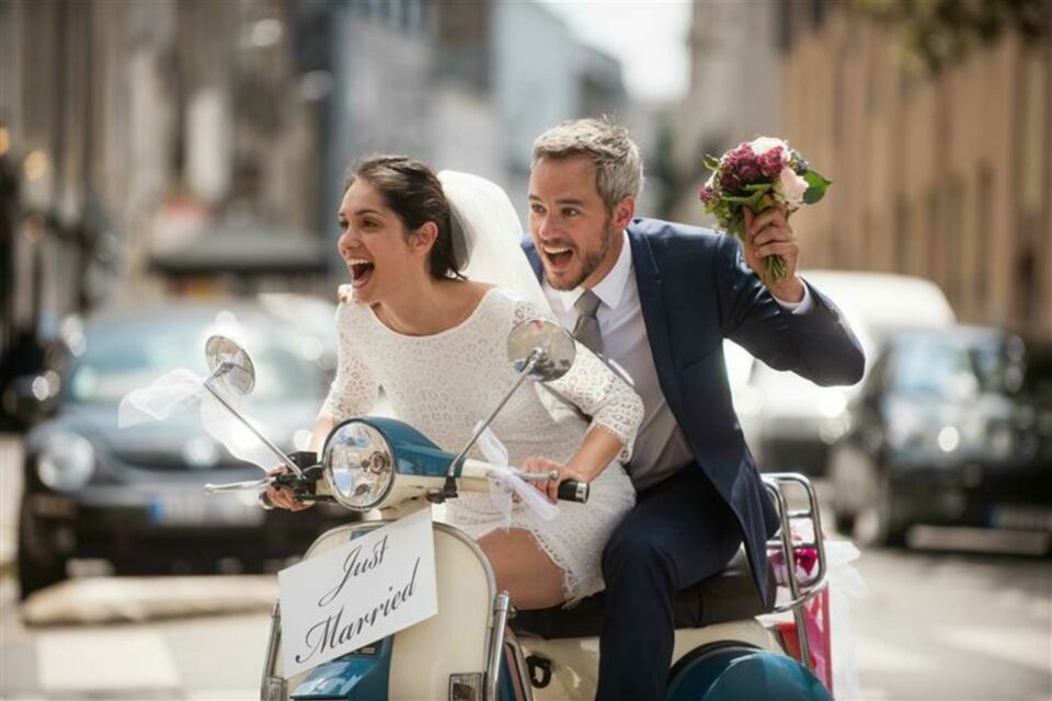 Adobe Stock - Photo d'illustration - Tout juste mariés, le couple file en scooter en tenue nuptiale, pour poursuivre leur mariage itinérant vers un autre lieu, symbole de liberté et d’aventure !&nbsp;