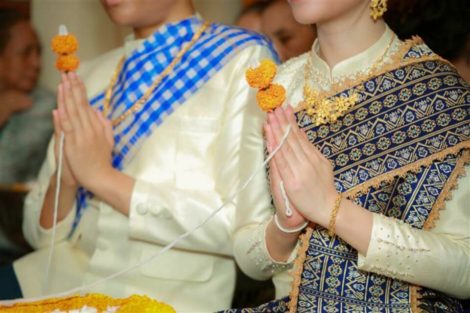 Adobe Stock - Photo d'illustration -&nbsp;Le couple de jeunes mariés entouré de leurs proches lors du Baci, le rituel du nouage des fils blancs autour des poignets, symbole d’union et de bénédictions partagées.