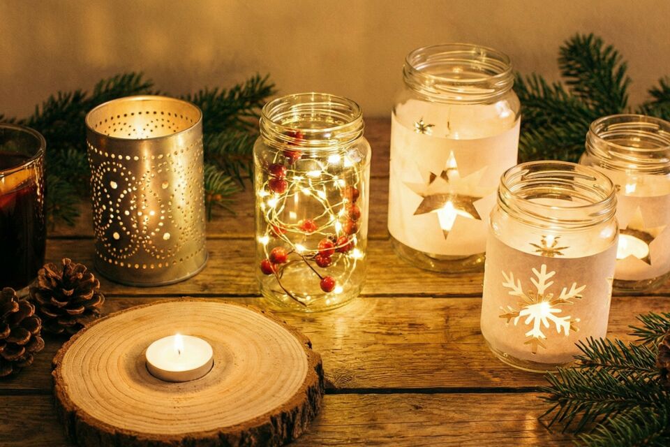 Gemini - Photo d'illustration -  Un ensemble de photophores artisanaux illumine une table décorée : verres givrés de sel, lanternes végétales et cocons de laine diffusent une lumière tamisée, chaleureuse et festive.