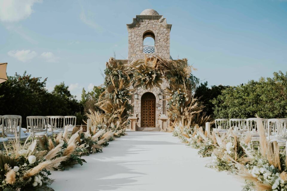 Pexels -&nbsp; Photo d'illustration -&nbsp;&nbsp;Allée de mariage bohème-chic menant à une chapelle coloniale en pierre au dôme à carreaux bleus, ornée de pampas, de fleurs et entourée d'arbres sous un ciel bleu clair