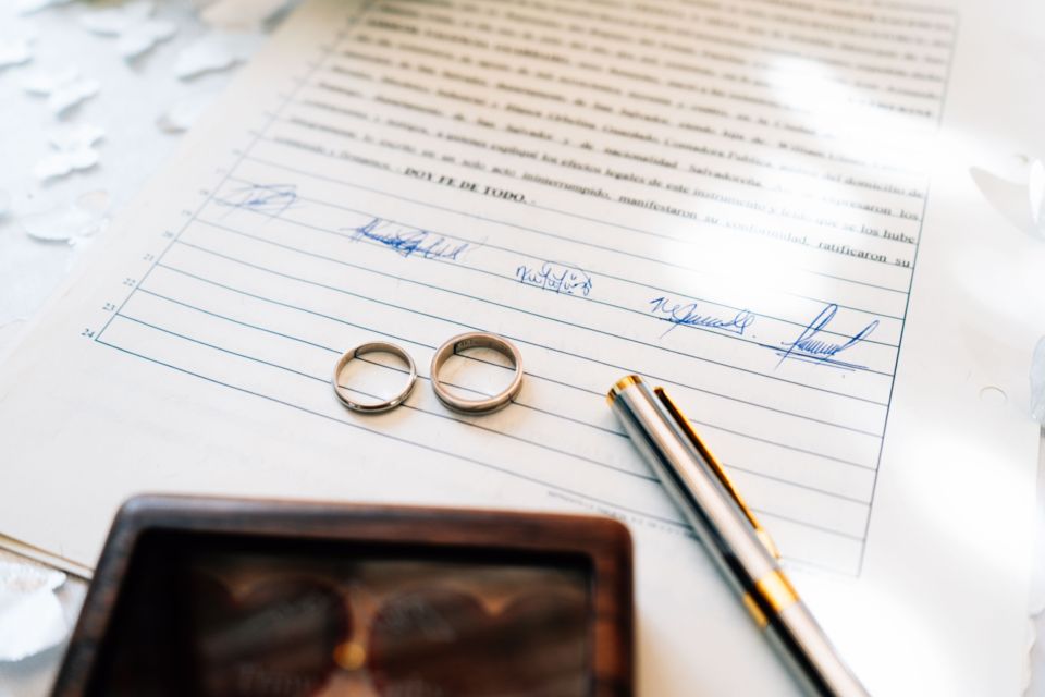 Pexels - Photo d'illustration - Une alliance posée sur un contrat de salle de mariage, symbolisant les engagements et les précautions indispensables à prendre pour protéger son événement face aux aléas et aux drames de la vie.