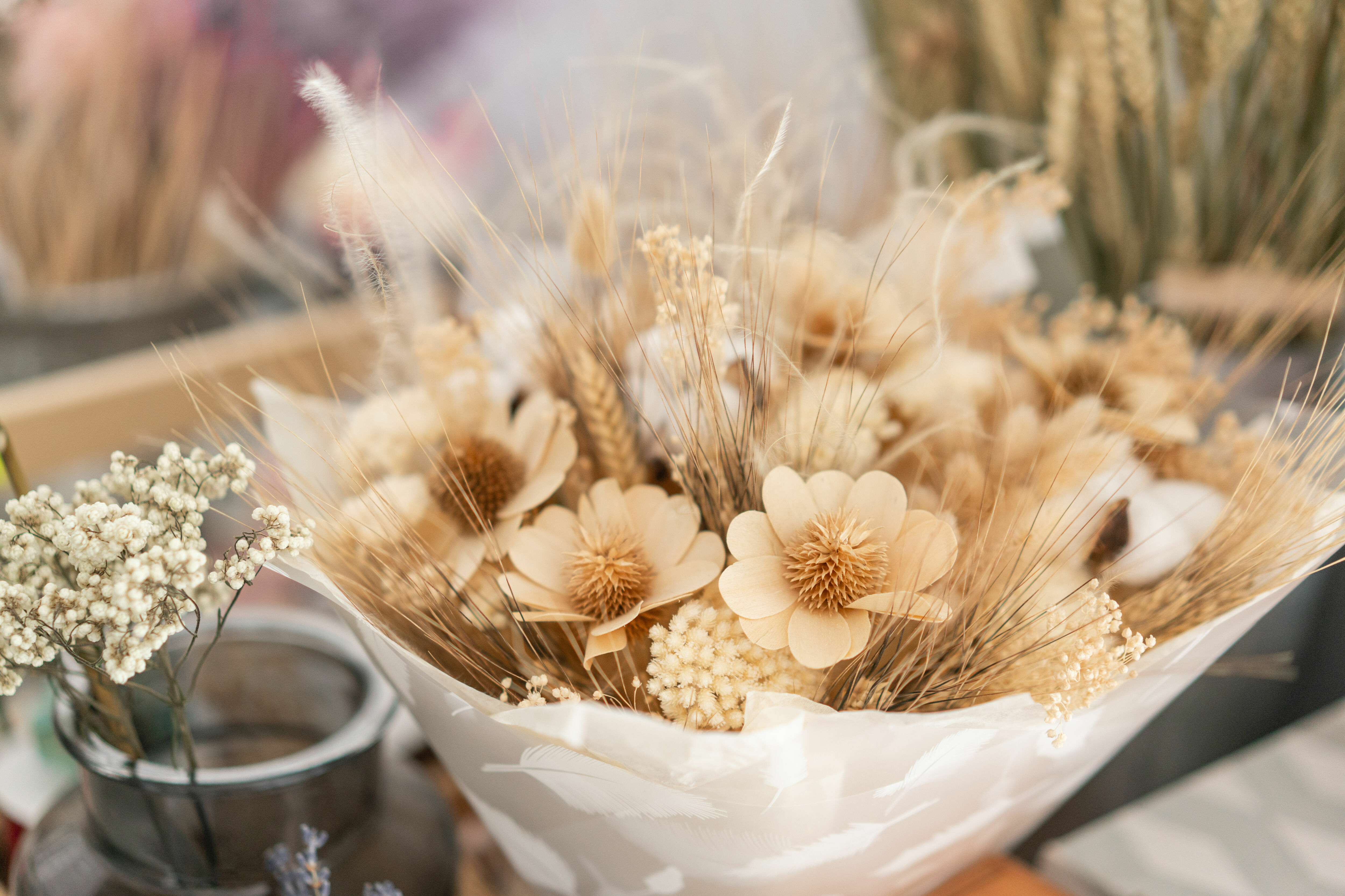 Adobe Stock - Photo d'illustration - Un bouquet de fleurs séchées beiges enveloppé par du papier de soie avec des motifs plumes.