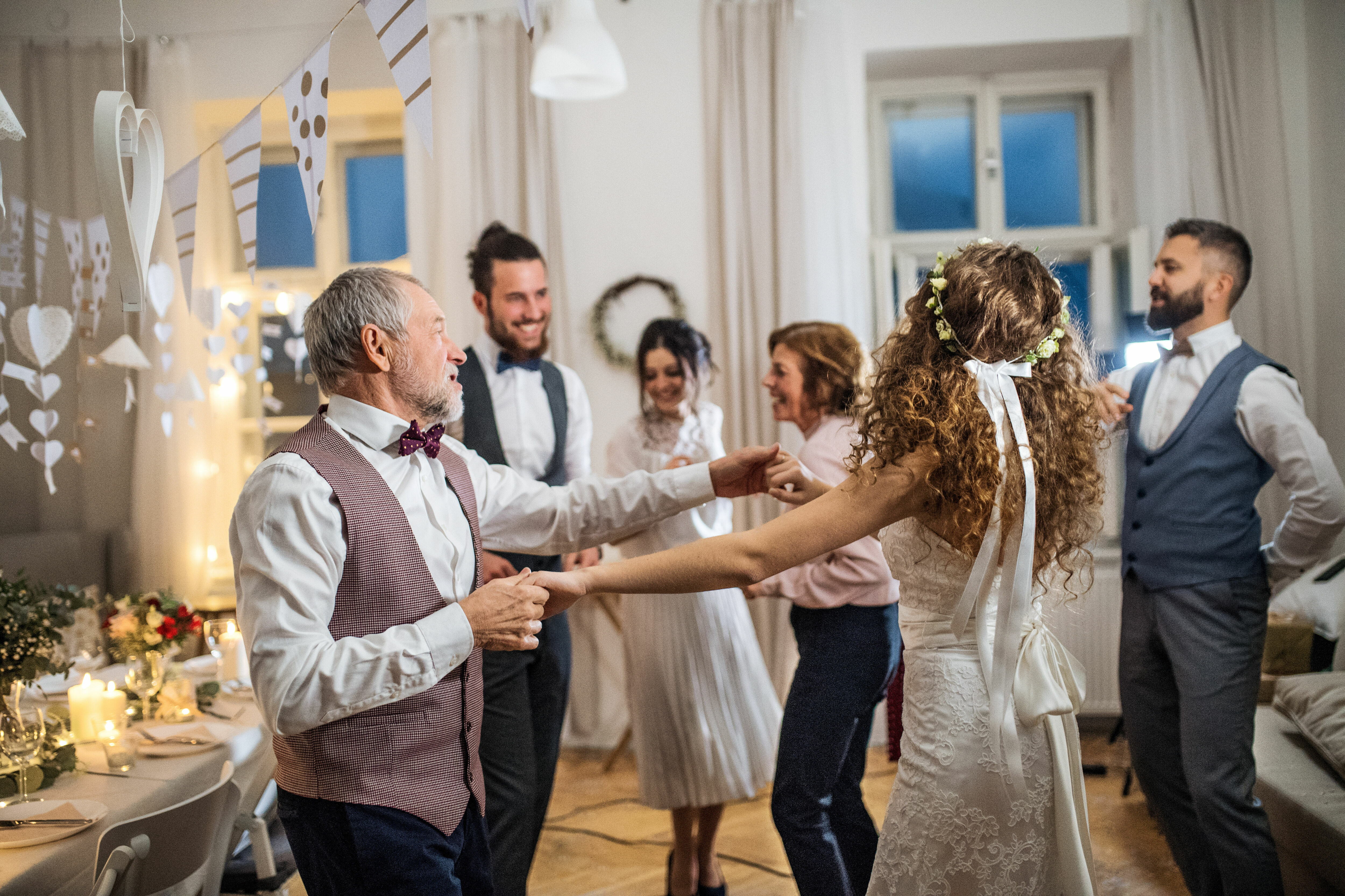 Adobe Stock - Photo d'illustration - Une jeune mariée, portant une couronne de fleurs, danse avec un homme qui pourrait être son père. D'autres membres de la famille dansent autour d'eux.
