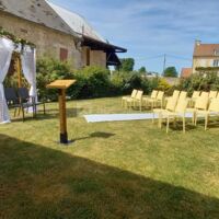 Cérémonie installée au jardin du domaine, chaises, tapis, arche, banc avec coussins
