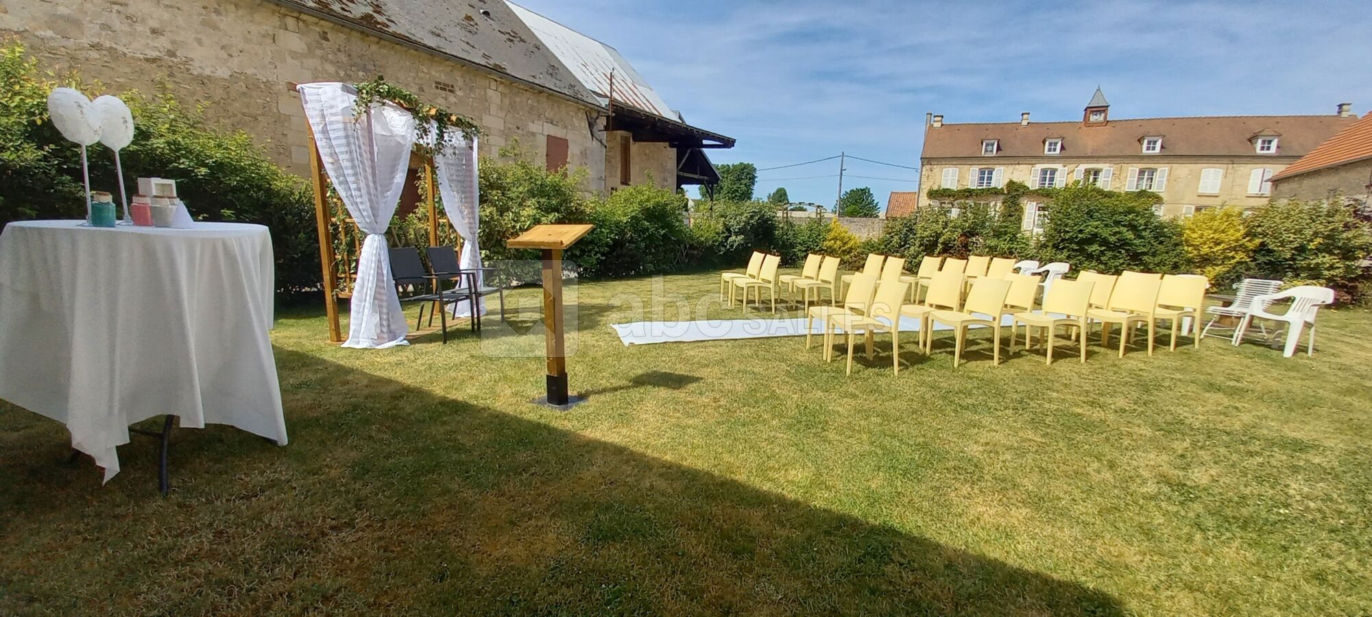 Cérémonie installée au jardin du domaine, chaises, tapis, arche, banc avec coussins