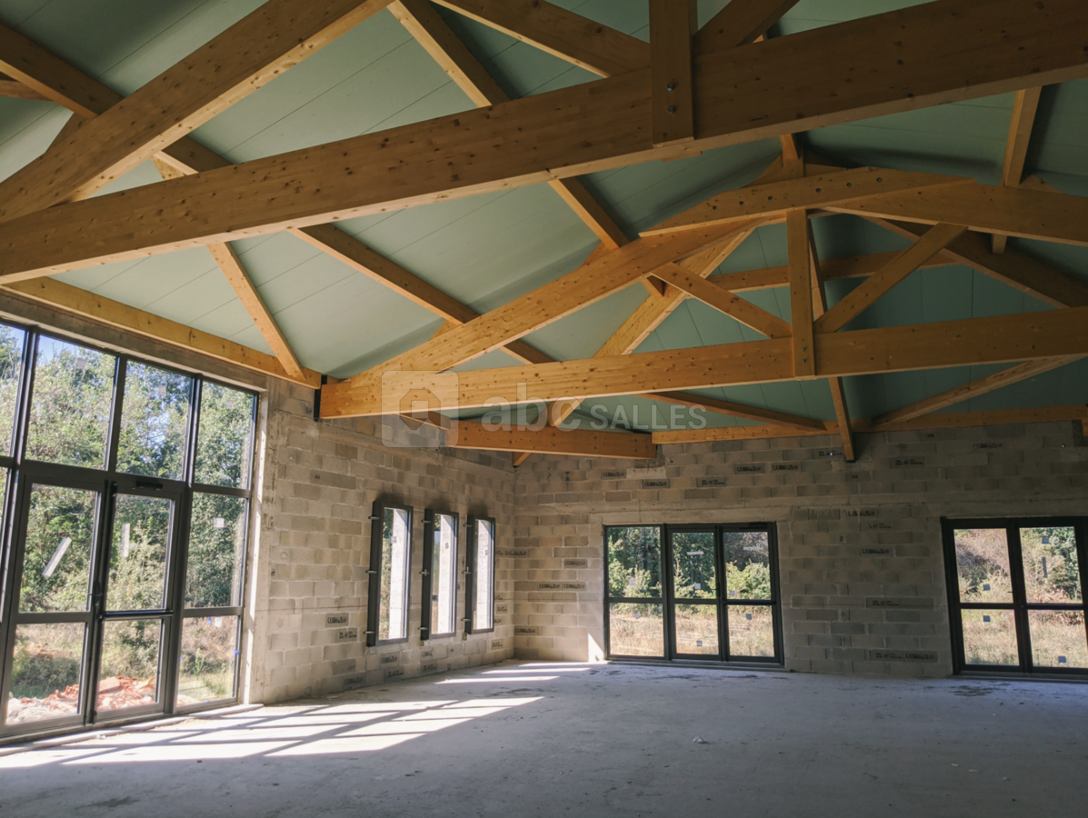 Intérieur avec charpente apparente et grandes baies vitrées pour faire entrer la lumière